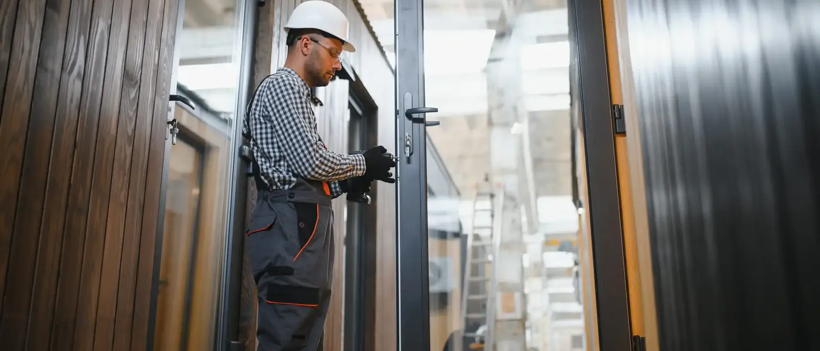 Technician fitting lock hardware on a tall aluminum-framed glass entrance door